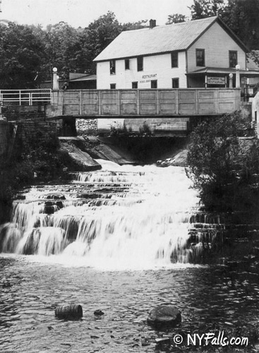 An old photo of Oriskany Falls from around 1935 showing an adjacent mill and a wooden bridge.