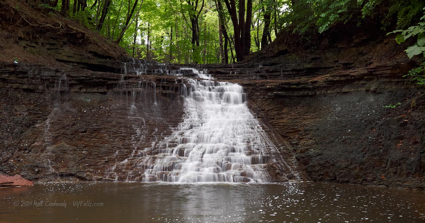 A head-on view of Densmore Falls showing a deep pool at its base and light wooded area above.