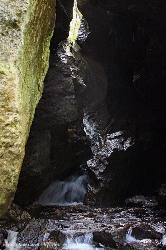 A view of Dover Stone Church that captures the waterfall inside as well as the tall wavy cliffs above.