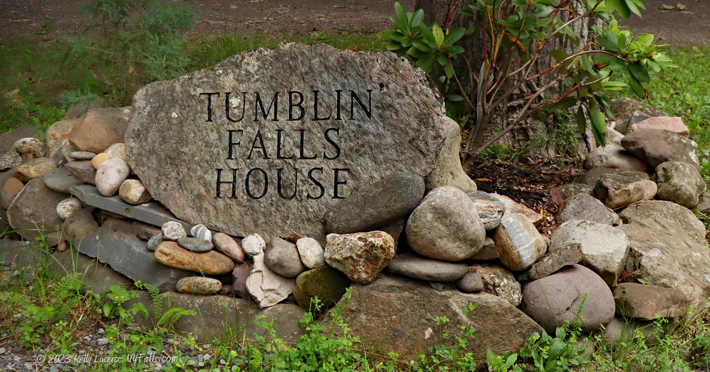 A large rock with the words Tumblin' Falls House neatly etched in capital letters - surrounded by many smaller rocks.