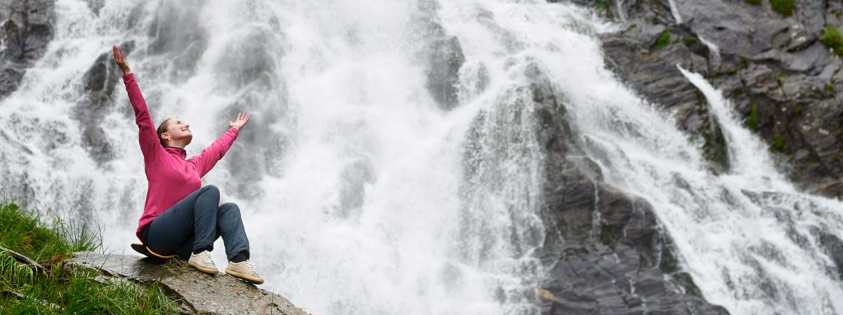 a cheerful woman in front of a waterfall (topic of waterfalls and mental health)