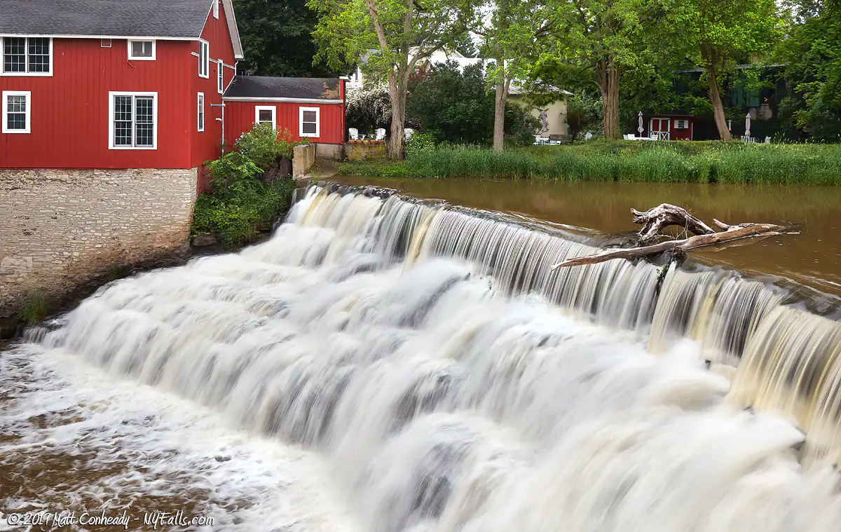 A closeup of Honeoye Falls showing an old tree stuck at the tope. In this view you can clearly see the top of the falls drops differently from the bottom 80% because the top is a dam and the bottom is a natural waterfall. In the top left is the old red mill.
