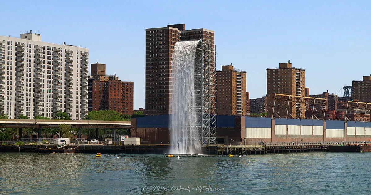A man-made waterfall along the east river in daylight. A part of the New York City Waterfall Project.