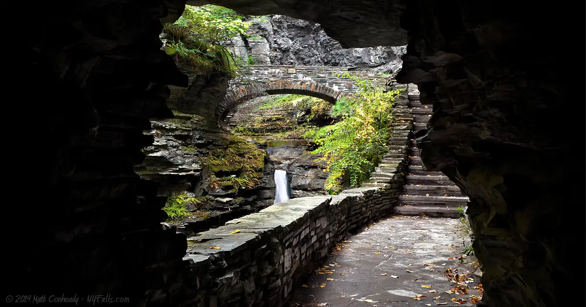 A view from within a cave, looking towards a bridge and waterfall in Watkins Glen