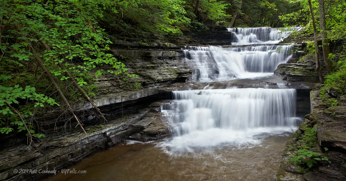 A view of a 3-tiered waterfall in a wooded section of Buttermilk Falls State Park.