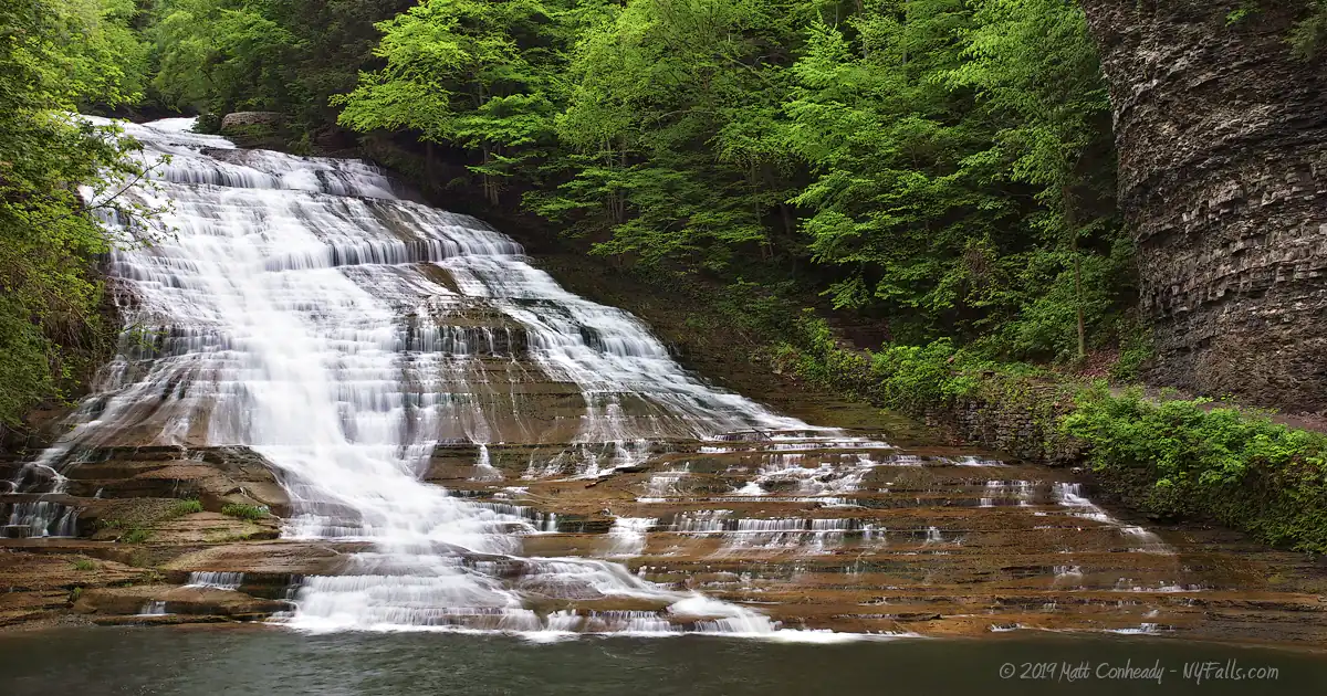 A wide view of Buttermilk Falls and a round section of a tall gorge wall to the right.