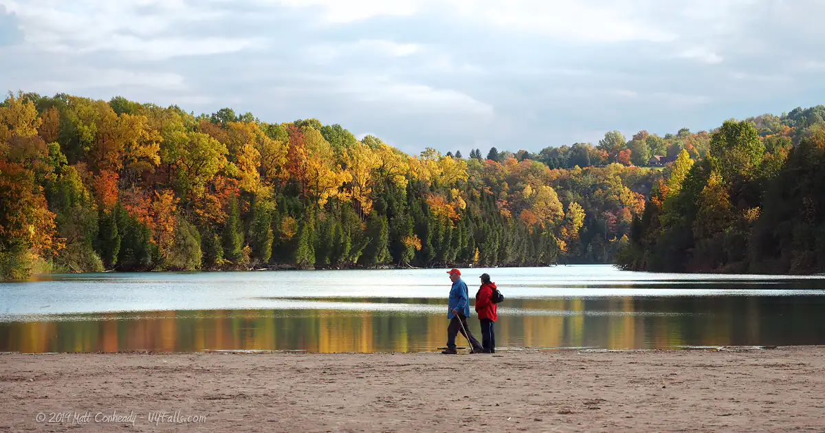 A couple walking across an empty sandy beach at Green Lakes State Park on a cold autumn day.