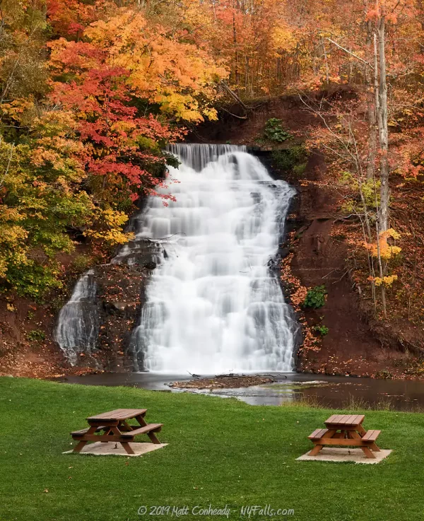 Two picnic tables in front of Holley Canal Falls in autumn.