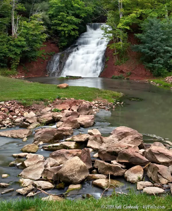 Holley Canal Falls in summer with very good waterflow. In the foreground is the East Branch of Stony Creek which has reddish stones piled in it to help direct flow.