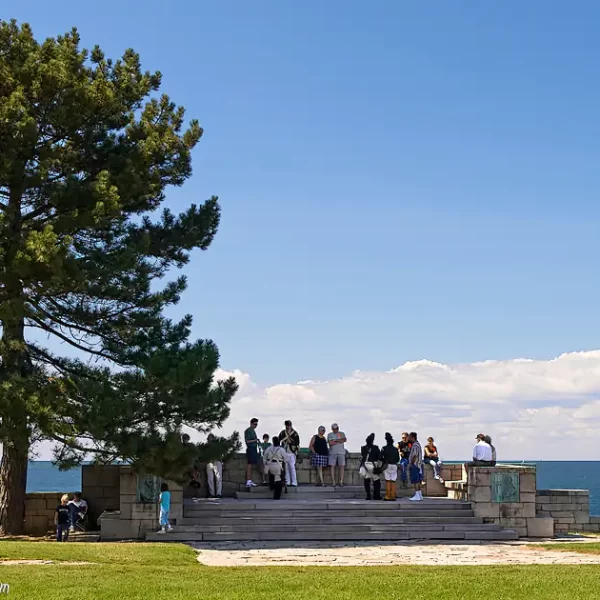 Visitors enjoying the shade of a large tree next to the Rush-Bagot Memorial at the Lake