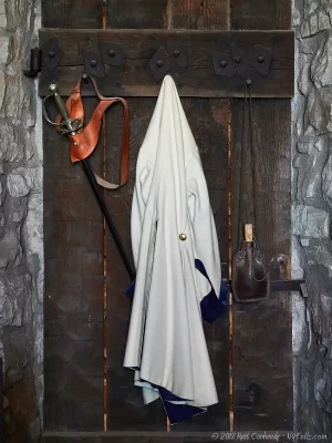 An officer's coat, sword, and canteen hanging on the back of his quarters door.