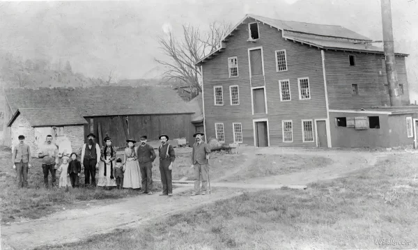An 1894 Black and white photograph of the Gibsonville Paper Mill. There are a number of people standing outside the mill, from L-R: Ben Stockings, John, Katie, and Jay Stocks, Ike Hoffman, Mrs. Frank Renney, Ike, Isobel, Willis, Frank Renney, Robert Ingersoll.