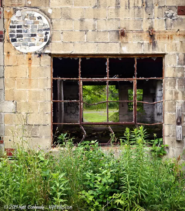 A broken window with bent frames on the abandoned Baker Chemical building at Cascade Mills