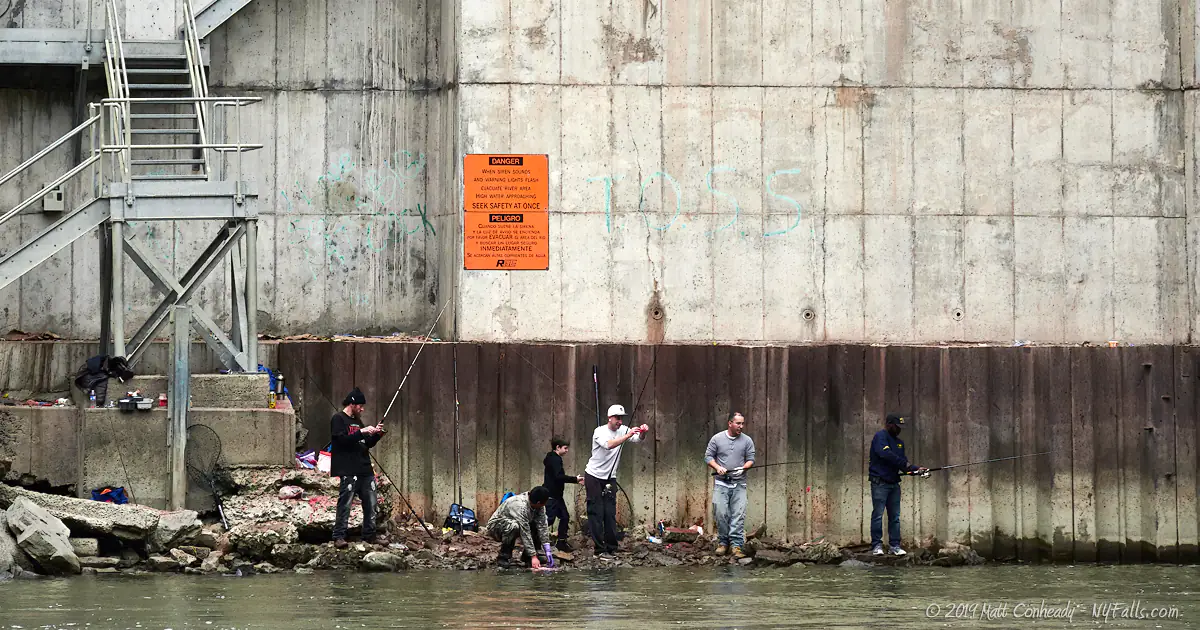 Fishermen standing on the shore of the Genesee next to the hydroelectric power facility at Lower Falls