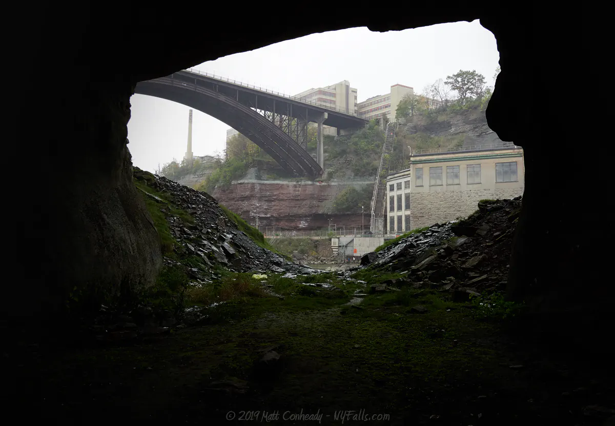 A view from the inside of the cave at Rochester's Lower Falls, looking out at the Driving Park bridge and a hydroelectric power plant.
