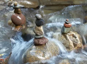 3 cairns made from pebbles standing on boulders in Stony Brook as water floods over.
