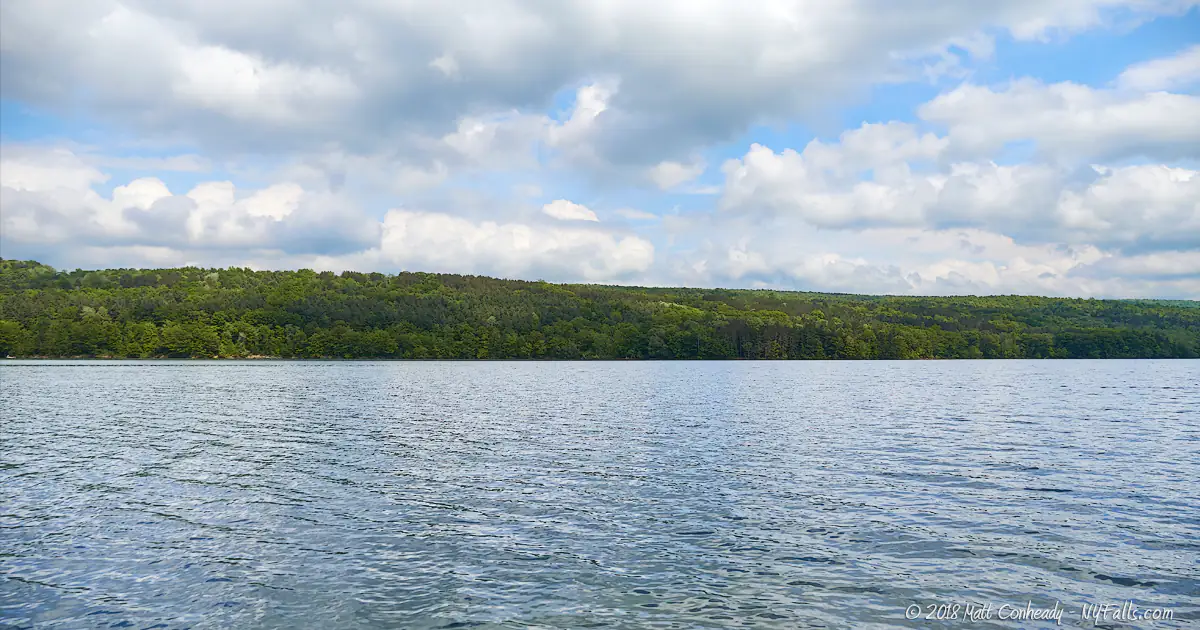 A panoramic view of Canadice Lake on a partly cloudy day.