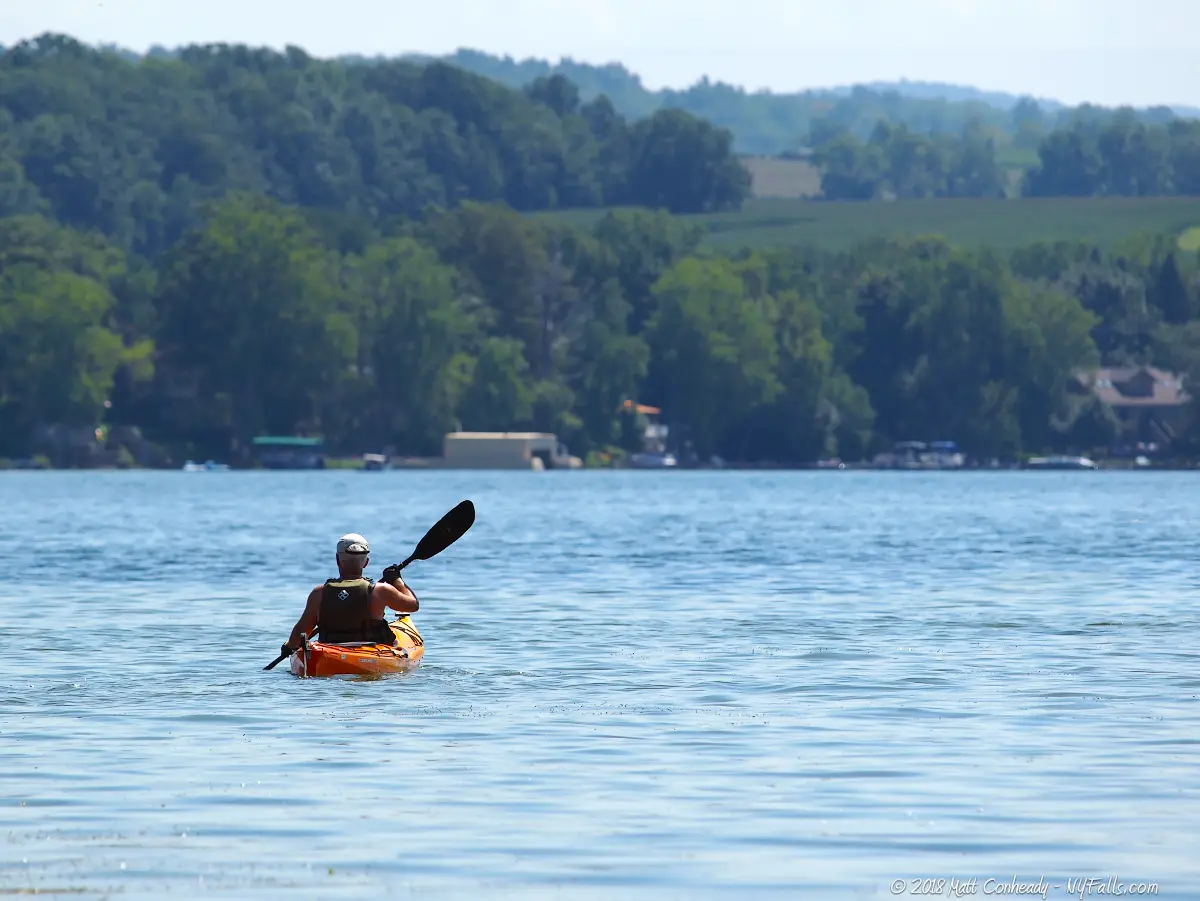 A Kayaker paddling across Conesus Lake on a sunny day.