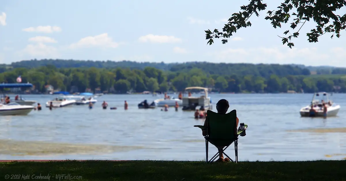 A person sitting in a lawn chair in the shade at Vitale Park on Conesus Lake