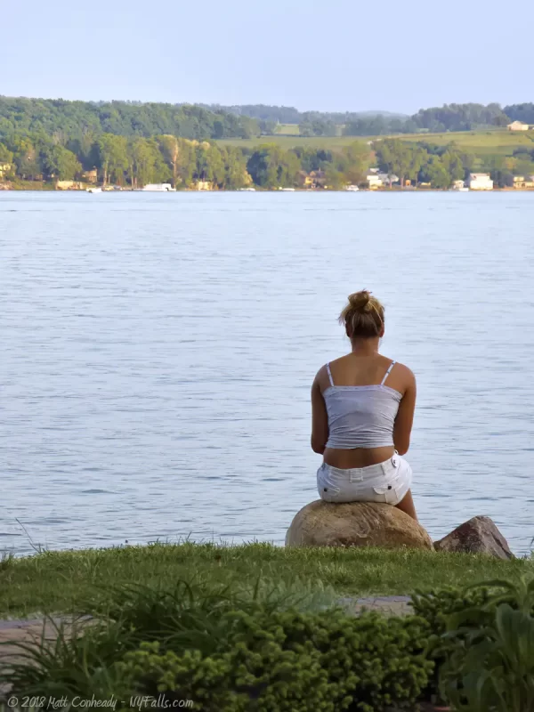 A woman sitting on a stone on the shore of Conesus Lake