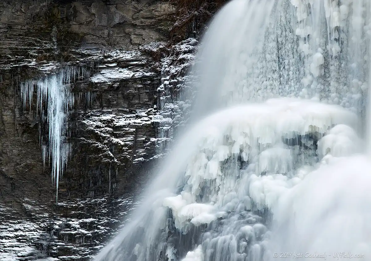 A closeup of Fillmore Glen's Cowshed Falls in winter. A large patch of icicles hands on the cliff next to the frozen waterfall.
