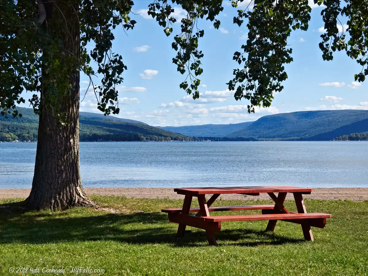 A picnic table at Sandy Bottom Park overlooks Honeoye Lake on a sunny day.