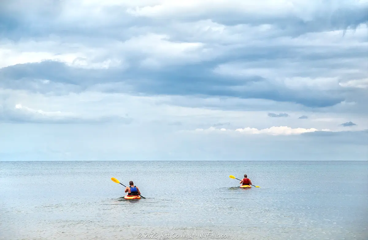 Two kayakers paddling out into Lake Ontario from the beach