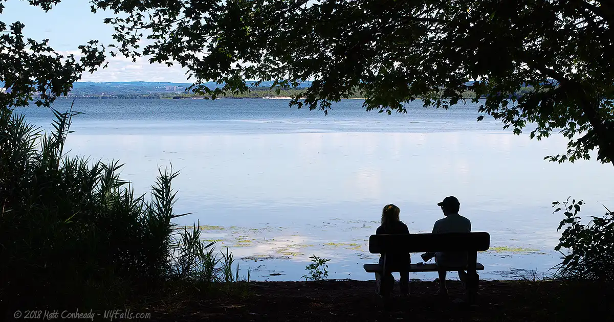A couple sits in the shade at the shoreline of Onondaga Lake