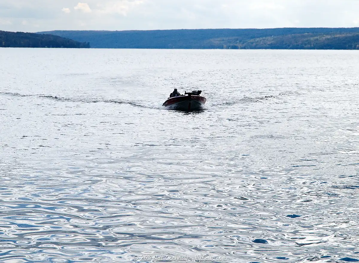 A motorboat moves across a blue Owasco Lake