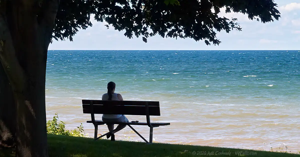 A woman sits on a becnh and enjoys the view of Lake Ontario from Barker Bicentennial Park.