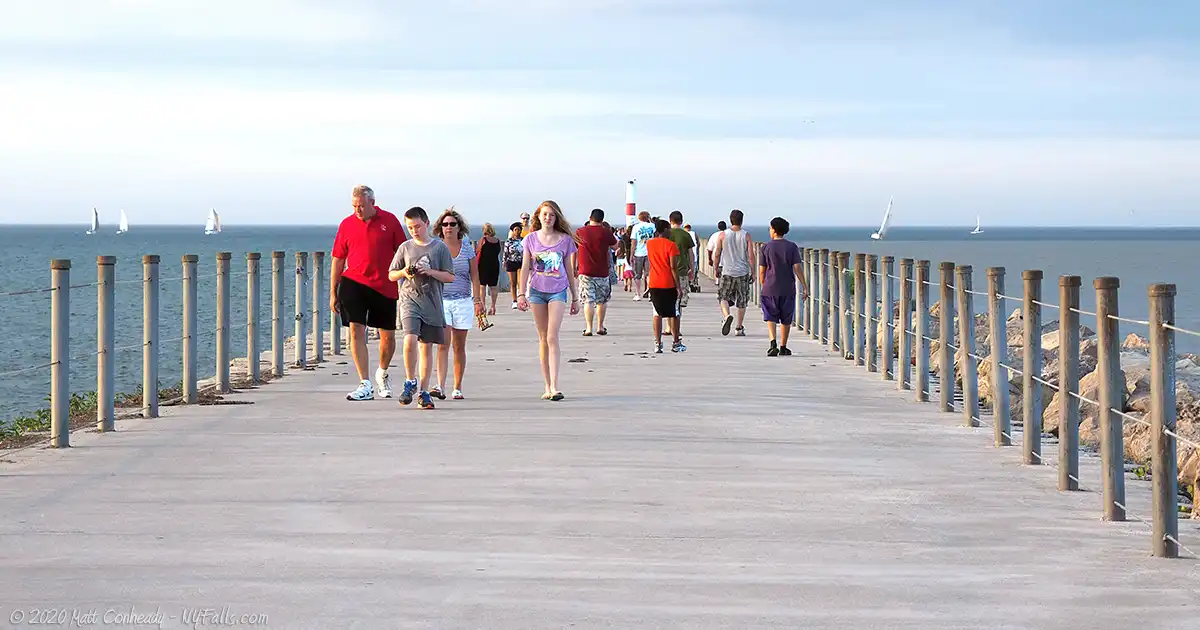 People walking up and down the Charlotte Pier at Ontario Beach Park.