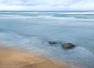 A slow shutter capture of the waves crashing on the sandy beach in daylight