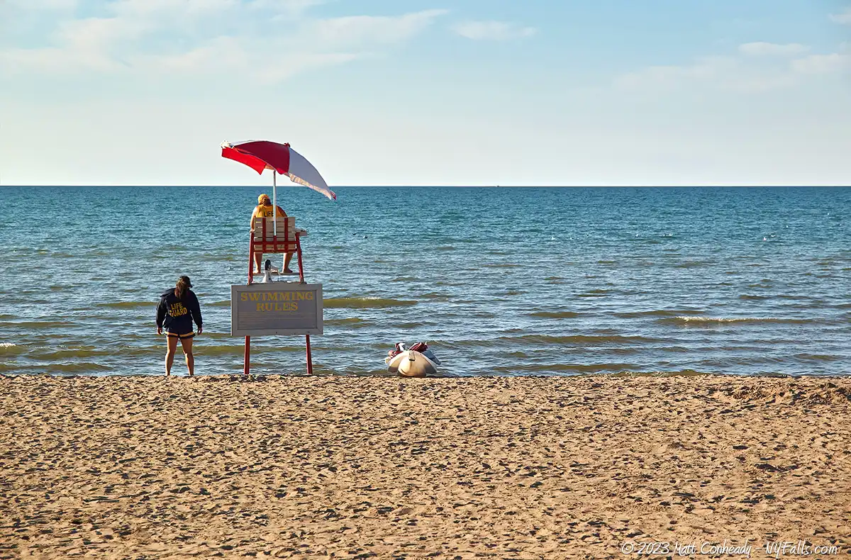 In the late afternoon sun, lifeguards are on duty, but there are no swimmers in the lake in front of them.