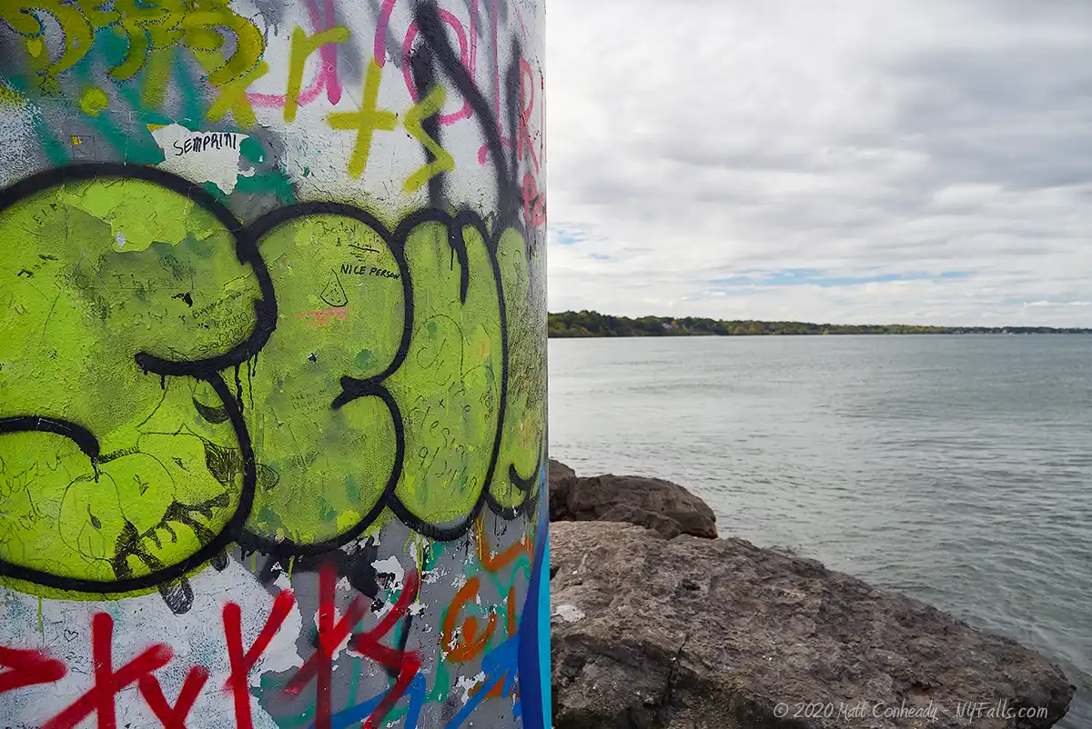 A view of the graffiti-covered beacon at the end of the pier and Lake Ontario in the background.