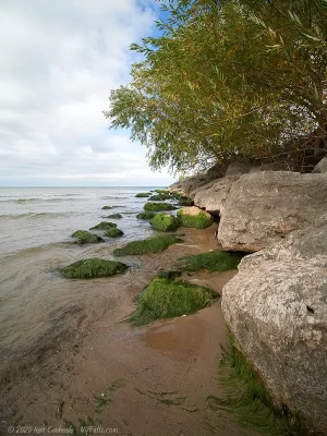 A view looking down the side of Seabreeze Pier, past algae-covered stones, out at Lake Ontario