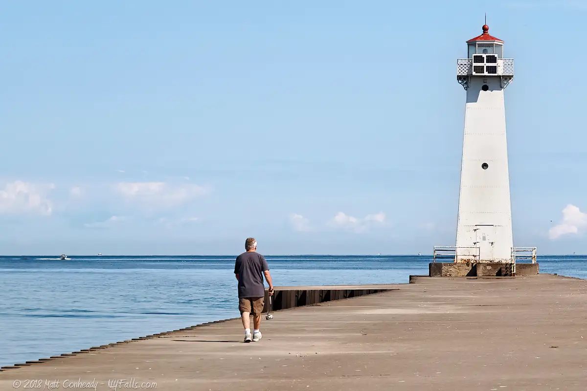 A man walking towards the end of the Sodus Point pier towards the beacon, which people often call the "lighthouse"