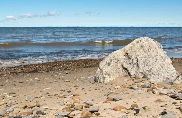 A large boulder embedded in the sand at the shoreline at the Lake Erie Seaway Trail Visitor Center