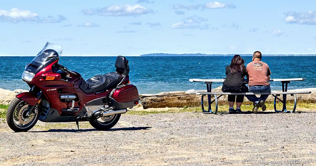 A couple takes a break from a motorcycle ride to sit at a picnic table and enjoy the view of Lake Erie from Hamburg Beach Town Park