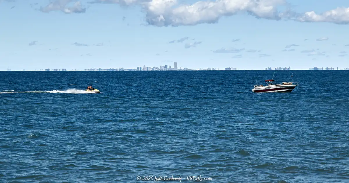 A boat and jetski on Lake Erie with the City of Buffalo visible on the horizon.