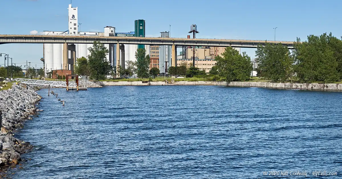 A view of a ship slip that borders Wilkeson Pointe Park, with the Buffalo Skyway, a garil elevator, and downtown buffalo in the background.