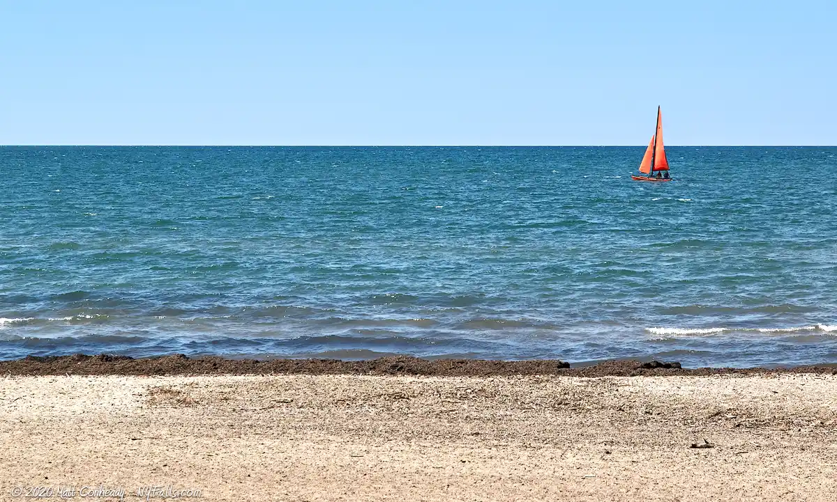 A sailboat with red sail passes the Beach at Hanover