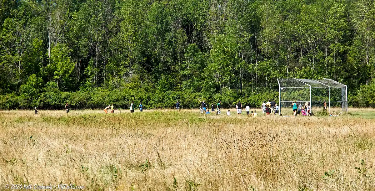 People playing a game of softball in a diamond surrounded by tall grass