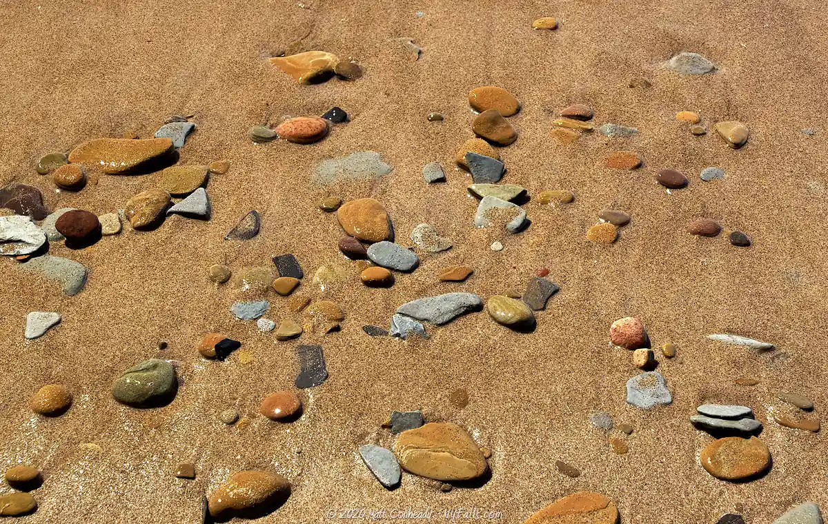 Golden brown sand and multicolored pebbles that make up the beach at Evangola State Park