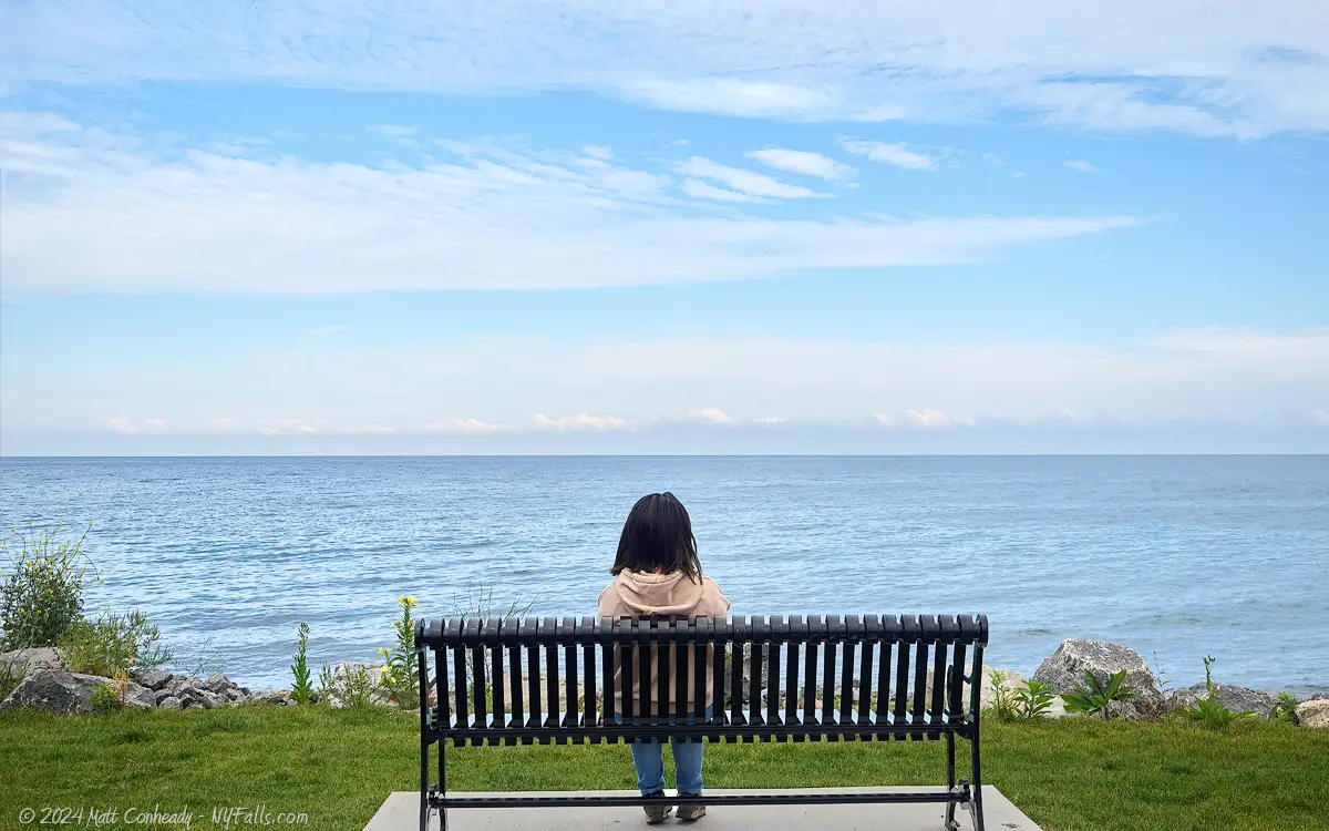 A woman sitting on a bench in front of Lake Ontario at Sheldon Beach Park in Oswego, NY